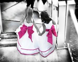 flower girls holding hands back of dressing with bright pink bows 