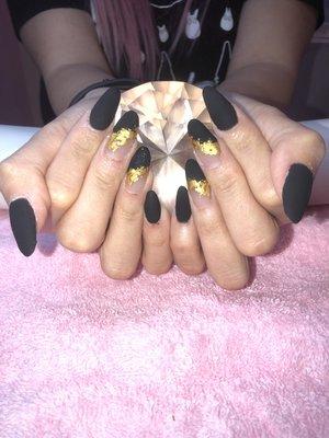 Matte black with gold foil accent on acrylic nails.