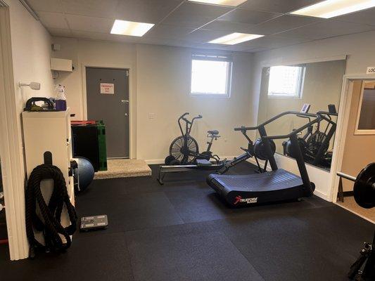 Secondary workout space with a Trueform motorless treadmill, rowing machine, and airdyne