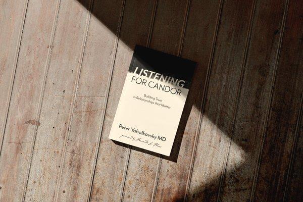 Picture of a paperback book laid on a wooden porch. The book is titled "listening for candor; building trust in relationships that matter"