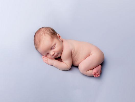 A simplistic portrait of a 1 week old baby photographed on a sky blue background.