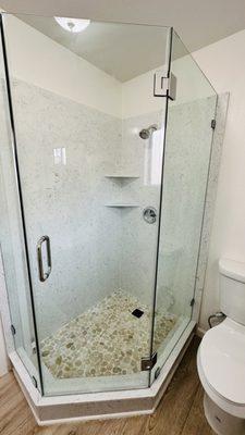 New stone panel shower surrounds with pepple stone and a custom frameless glass door.