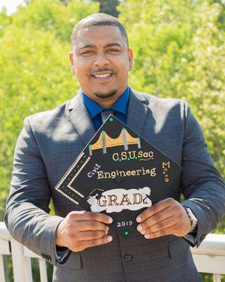 Smiling graduate holding decorated cap, wearing a suit, captured in Sacramento by Cherish the Moment Photography.