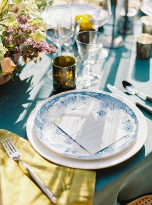 a luxury intimate tiny wedding tablescape with deep blue linen flowers candles and custom menu