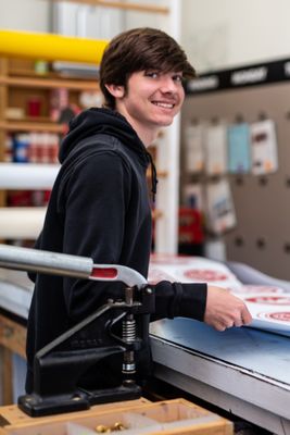 Dedicated craftsmanship in progress! Witness one of our talented sign shop employees meticulously crafting signage at the table