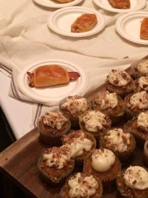 Carrot cake cupcake with cream cheese icing topped with pecans and a bacon wrapped croissant.