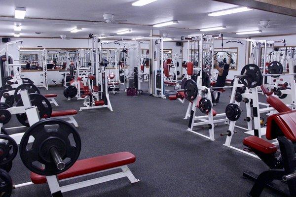 Huge free weight room with new equipment: bench presses, squat racks, incline bench, decline bench, cables, and overhead press.