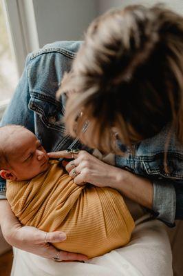 Mom is enjoying the sweet and tiny features of her newborn baby all swaddled up in his nursery