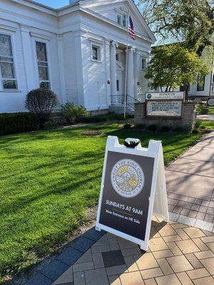 Front of the church with directional sign that points people to north east side of the building for main entrance.