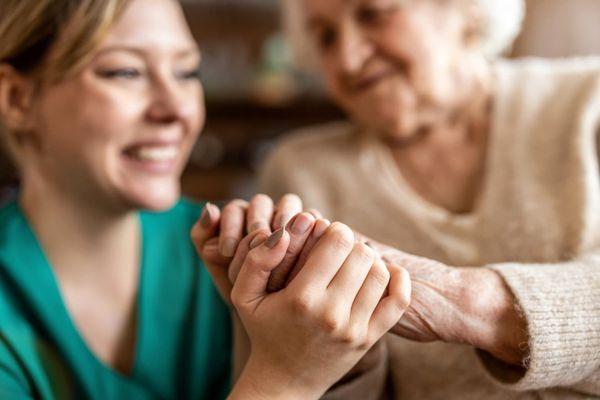 Homecare worker and a senior aging adult holding hands