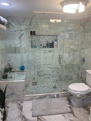 Custom marble shower with large bench seat, niche, and frameless shower glass.