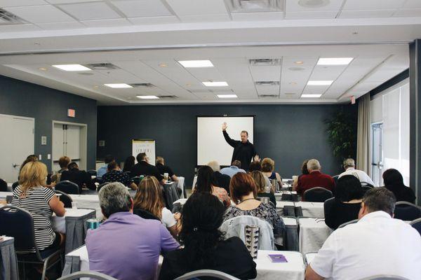 Tony Daum communicating infront of a full room at an Excellence Performance Seminar.