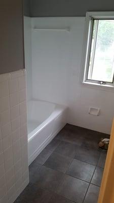 Reglazed wall tiles and bathtub in white, painted walls and ceiling, and installed groutable vinyl floor.