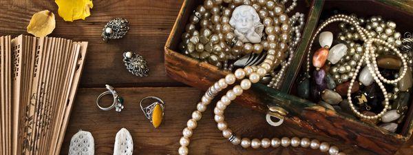 open jewelry box with pearls, stones, and angle piece and various other trinkets laid out on a wooden table