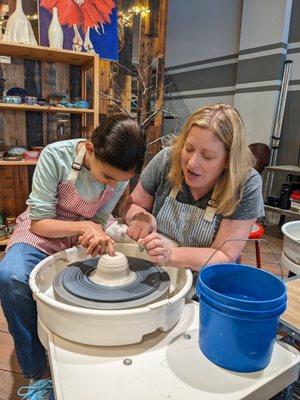 Holly works with a young artist on the pottery wheel.