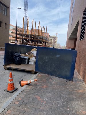 Dumpster parked in vehicle parking, trash flying everywhere, and dumpster literally blocking public sidewalk.