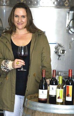 Winemaker, Megan, in the cellar posing with some of the bottles of wine she proudly made.