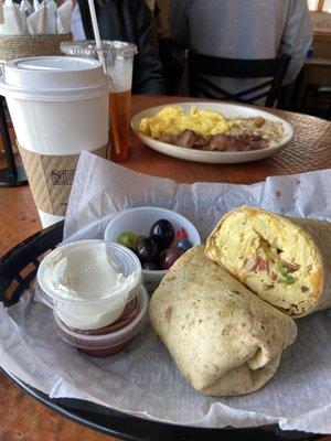 Breakfast burrito and eggs,bacon, hash browns behind! Nice little bowl of fruit and salsa/ sour cream with the burrito.