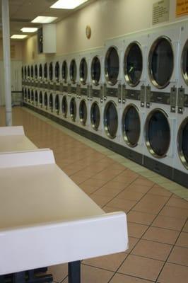 Wall of industrial driers. You can fit a lot of stuff in those. Left: folding tables at the end of a row of washing machines.