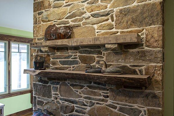 Reclaimed beam and live edge shelves rest on stone corbels of chimney center piece in this great room.