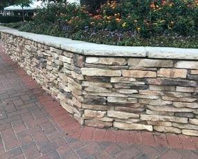 A stacked stone retaining wall with a landscaping bed feature inside.