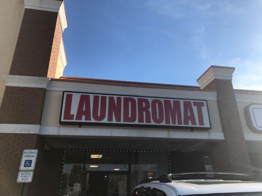 Front of laundromat in strip mall - to the left (facing sign) is a dry cleaners, and to the right is a nail salon.