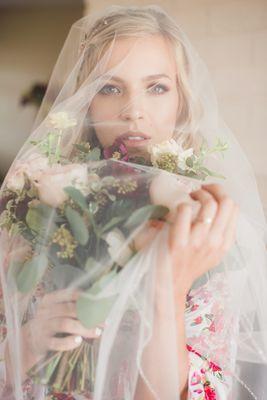 a bride looking dramatically at the camera with her veil over her head and a bouquet in her hand