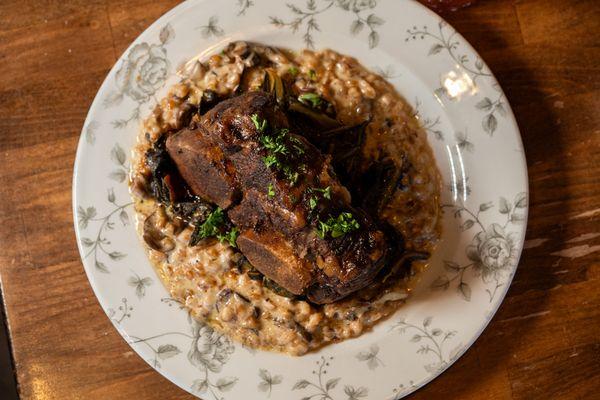 The Short Ribs. 16oz Bone-In Beef Short Ribs. Falls Right off the Bone! Served with Cheesy Farro and Mushroom Risotto and Collard Greens.