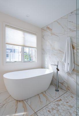 A serene oasis featuring a standalone tub surrounded by marble tiles that reflect natural light.