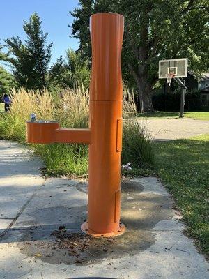 Drinking fountain. Basketball court in the background.