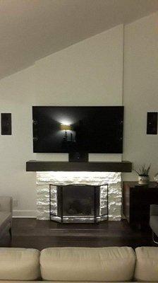 Mounted TV over fireplace w/hidden wires as well as installed speakers on side of TV on wall.