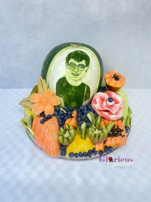 Custom carved watermelon for a birthday party with a carved face of the boy and fruit arrangement