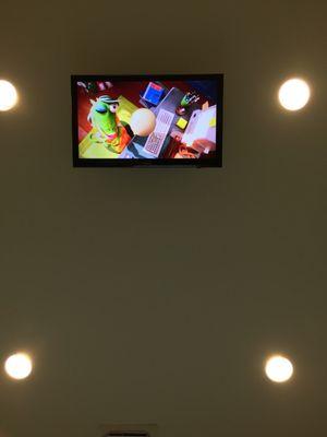 The ceiling-mounted television playing "Sing" through Netflix.