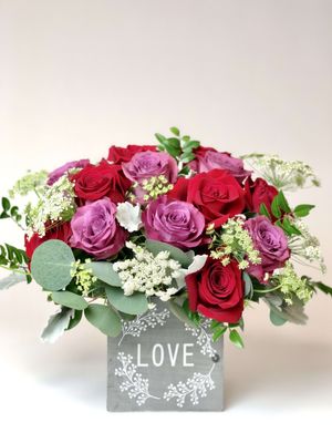 Modern Rose design in red and lavender with Queen's Lace, eucalyptus and greens in collectible container