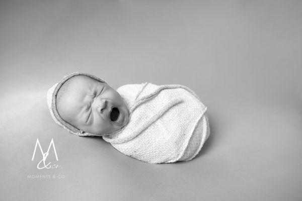 Newborn boy yawns wrapped on a blanket in black and white