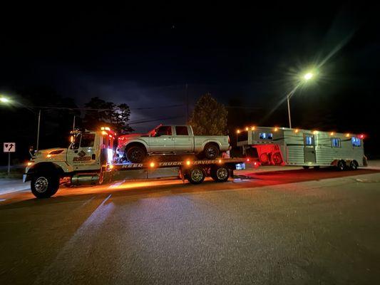 Tow truck with F250 on the bed, pulling a gooseneck horse trailer.