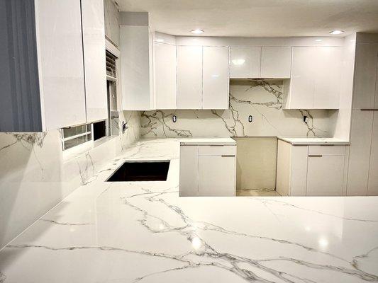 Glossy White European Style Cabinets and Pegasus Quartz Full Backsplash with Wrapped window wall.