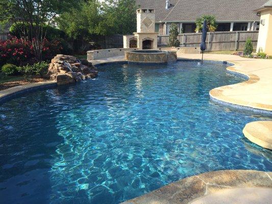 A Trinity Valley Pools custom in ground swimming pool, spa, in-floor cleaning and circulation system, waterfall and fireplace.