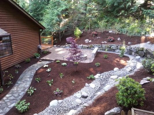 This landscape renovation included a new patio, fire pit, sitting wall, dry creek bed, landscape lighting, and planting beds ...