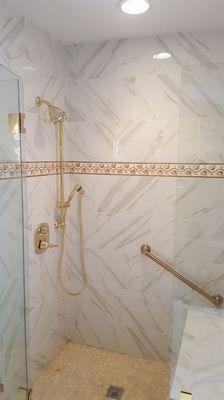 Heated shower pan and bench and bench wall. Porcelain tile calcatta marble look with travertine listel, river rock floor.