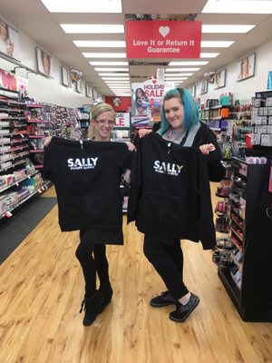 Two Beauty Consultants, both certified in hair color, holding up their matching Sally hoodies