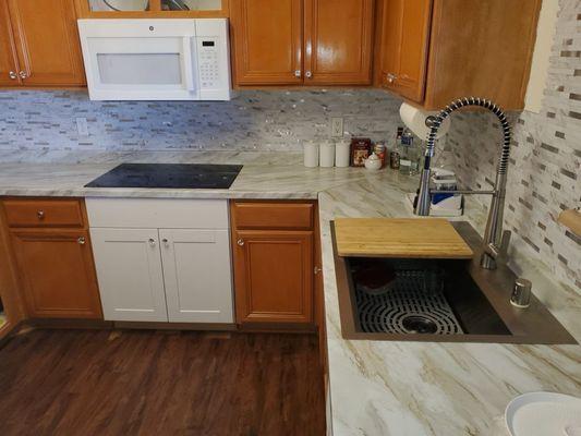 This photo shows the renovated kitchen with a new cooktop, countertop, sink, and all-in-one microwave with vent.