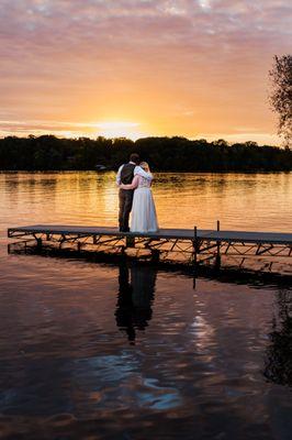 A Bride and Groom pose on a dock, watching the sunset during their wedding day.