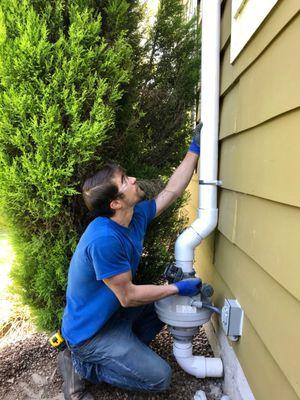 A team member securing a Radon mitigation system to the exterior of a client's house.