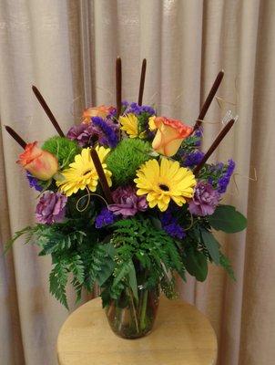 Flowers with cattails, roses, gerbera daisies and purple carnations.