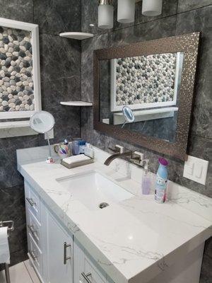 Master vanity in quartz slab, 24x24 porcelain tiles around the walls, frame picture on the wall with pebbles tiles.