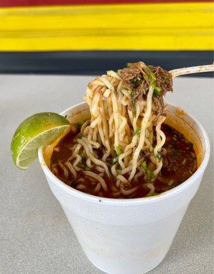 Birria ramen soup. The birria soup is loaded with ramen , onions cilantro and meat with lime on the side