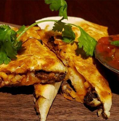 Jerkadilla is a Flour Tortilla filled with Cheddar Cheese Jerk Chicken Rice and Peas Drizzled w/Jerk BBQ sauce  and Mild Cilantro Salsa.