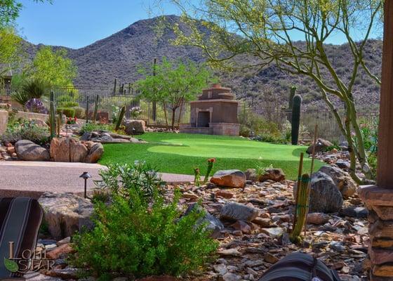 Desert landscape with artificial turf putting green and seating area with fireplace.