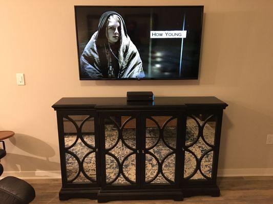 55" TV mounted above large cabinet. Wires concealed.